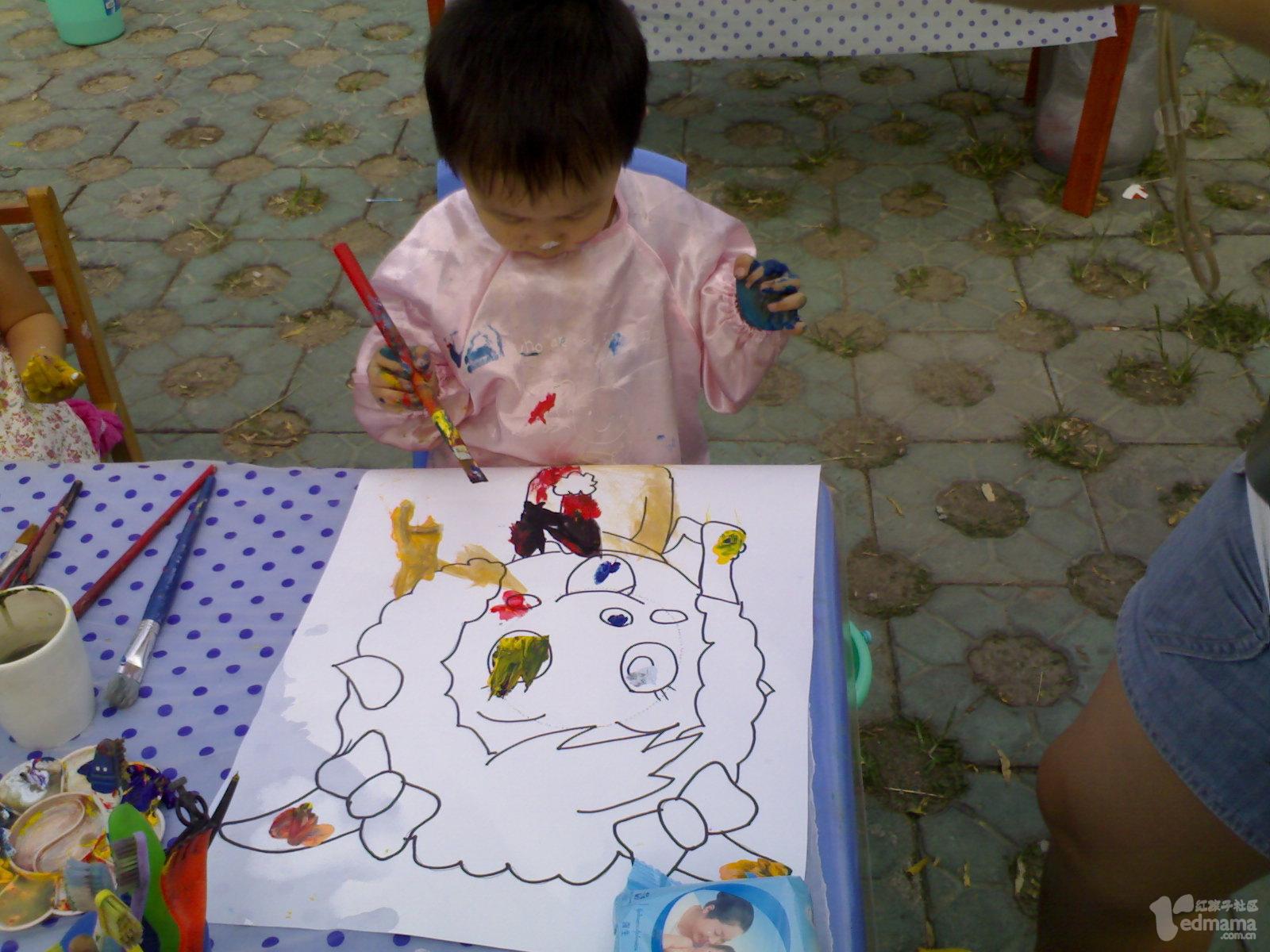 3岁的豆豆给美羊羊涂色，每个宝宝都有一张图画，颜料盘，笔和水杯，将自己与所涂鸦的作品拍照。豆豆戏称：“我把美羊羊给涂成了灰太狼!”。