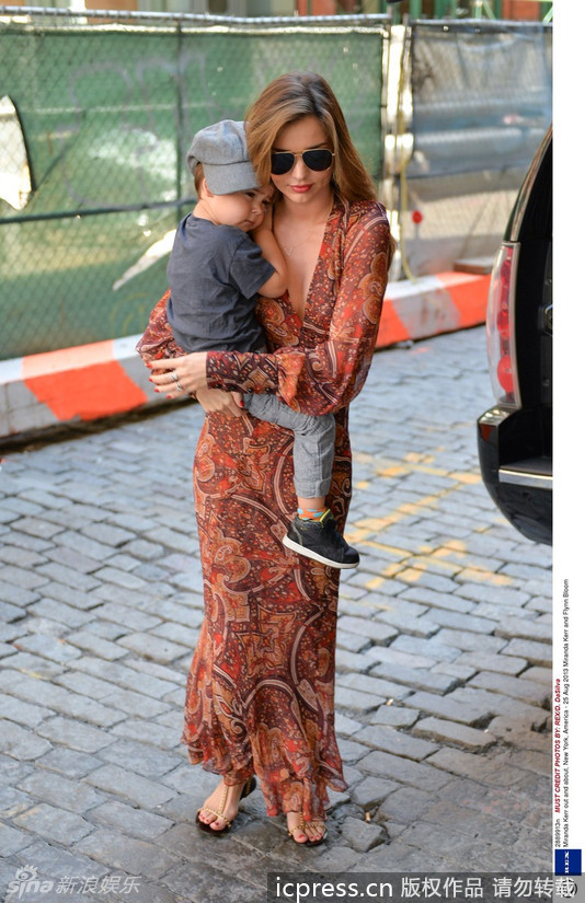 米兰达-可儿(Miranda Kerr)一袭红色长裙走在纽约大街上，露出深V胸线，手紧紧搂着儿子，母爱泛滥，小宝贝静静地伏在妈妈的肩头上。