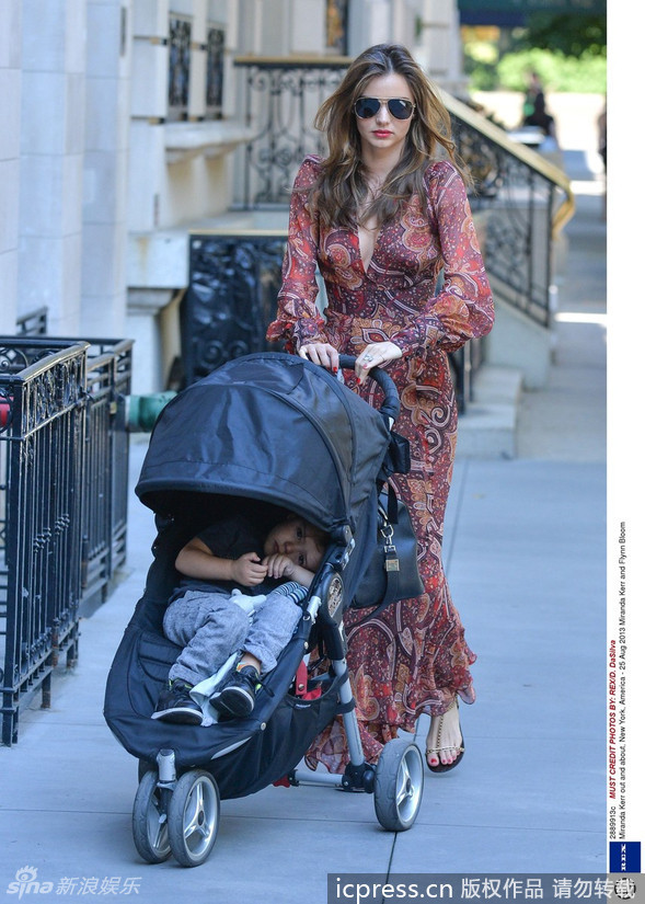 米兰达-可儿(Miranda Kerr)一袭红色长裙走在纽约大街上，露出深V胸线，手紧紧搂着儿子，母爱泛滥，小宝贝静静地伏在妈妈的肩头上。