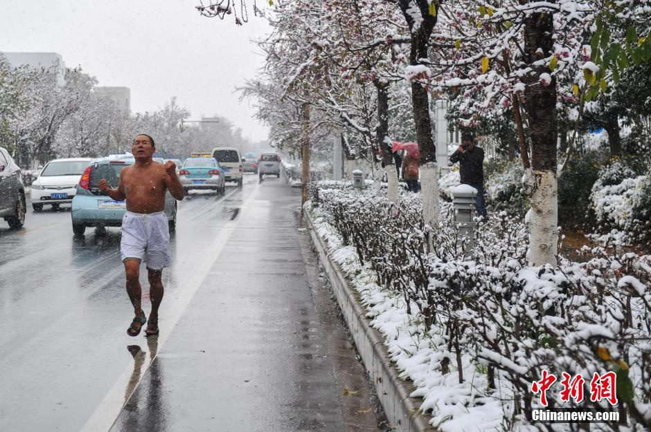 2013年12月16日，昆明城区降下今冬首场雪，对于多年不见雪花的昆明市民来说下雪就像过节一样，随处可见顶风冒雪的民众在路边拍照，玩雪。图为一男子脱光上衣在雪中跑步。