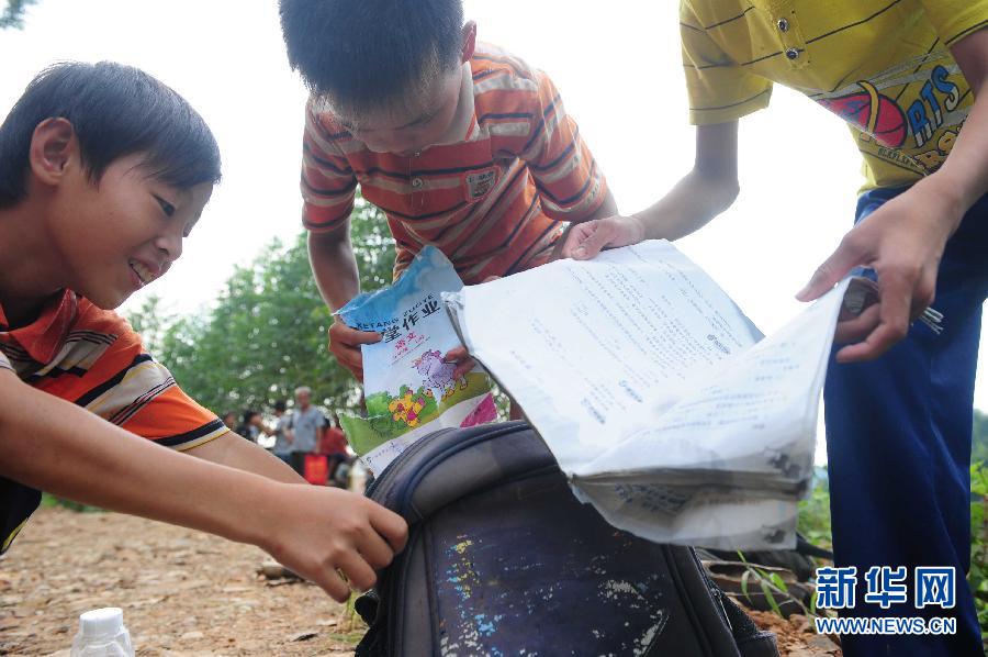 9月9日，在广西藤县古龙镇陈平村小学通往那龙组的桥上，放学回家的孩子们涉水通过桥面后，书包里的课本被水浸泡。