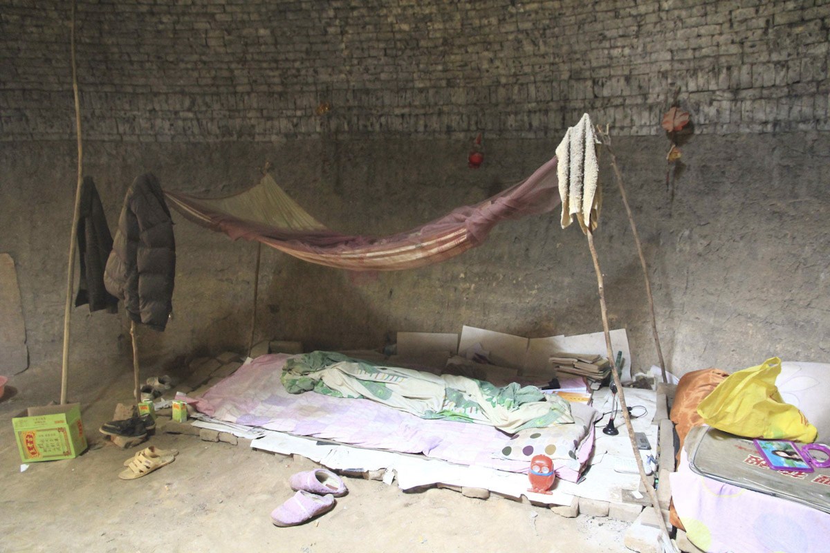 2013年9月16日，河南省郑州市，老张的住所紧靠西侧洞壁下，是一处地铺，支着一顶旧蚊帐，支蚊帐的木棍上，挂着一些旧衣服。地铺旁边，堆着一些杂物，上面落满灰尘。