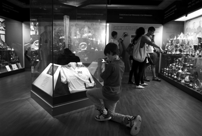 　　曼联博物馆内，一名小球迷单膝跪在地上拍摄曼联名宿博比·查尔顿参与奥运火炬传递时的火炬以及当时穿的005号火炬手服。 