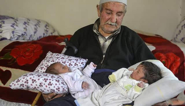 照片中的老人来自土耳其，85岁，名叫AbdullahSevinc。怀中抱的两个孩子竟然是他的孩子。这是老人第十四和第十五个孩子，两个孩子同一天来到世上，他们是双胞胎。老人与前妻生育10个孩子，前妻去世后，老人娶了小39岁的现任妻子，两人之前生育3个孩子，现在又生育一对双胞胎，而此时现任妻子已经46岁。老人和孩子们，他们生活在一栋破旧房子里。老人表示很难为情，自己最大的孩子已经60多岁，不过仍然很高兴。老人老来得子，现在最大的麻烦是如何养育孩子们。老人明确表示15个孩子足够多了，以后将不再生育。