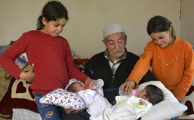 照片中的老人来自土耳其，85岁，名叫AbdullahSevinc。怀中抱的两个孩子竟然是他的孩子。这是老人第十四和第十五个孩子，两个孩子同一天来到世上，他们是双胞胎。老人与前妻生育10个孩子，前妻去世后，老人娶了小39岁的现任妻子，两人之前生育3个孩子，现在又生育一对双胞胎，而此时现任妻子已经46岁。老人和孩子们，他们生活在一栋破旧房子里。老人表示很难为情，自己最大的孩子已经60多岁，不过仍然很高兴。老人老来得子，现在最大的麻烦是如何养育孩子们。老人明确表示15个孩子足够多了，以后将不再生育。