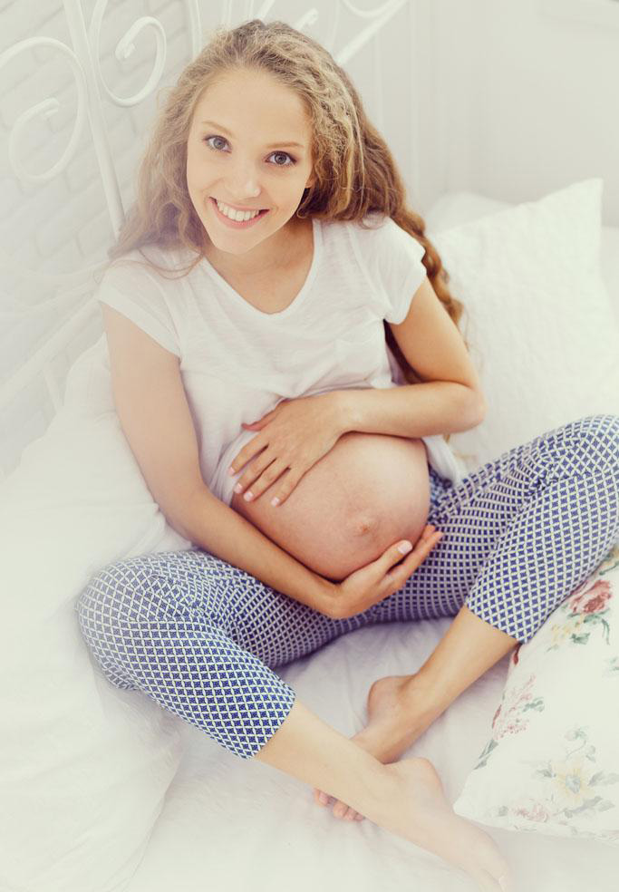 抱着肚子的孕妈妈超级的美啊，坐在床上的她温柔的呵护肚子里的小宝贝，笑容灿烂迷人。长卷发的她超级的美呢。尽管怀孕，但是瓜子脸的她越发的美了~~